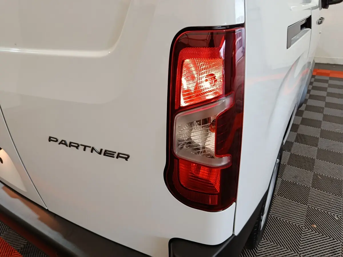 Gros plan sur le feu arrière droit d’un Peugeot Partner blanc XL 950kg, avec logo visible sur la porte arrière.