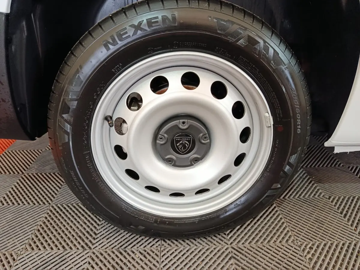 Gros plan sur la roue avant droite du Peugeot Partner blanc 2025 avec jante acier et logo Peugeot au centre.