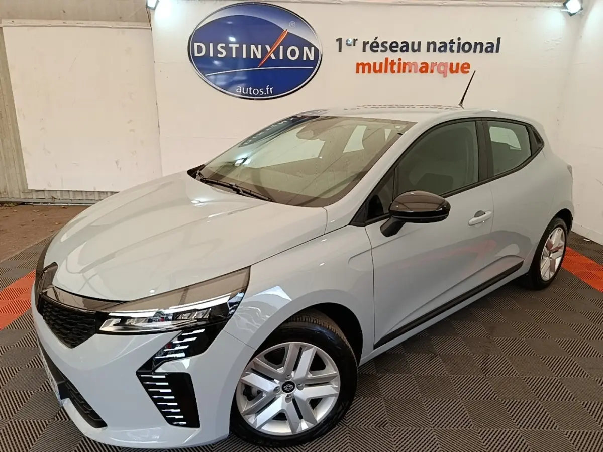 Renault Clio gris clair vue 3/4 avant droit en intérieur avec feux LED et jantes alliage visibles.