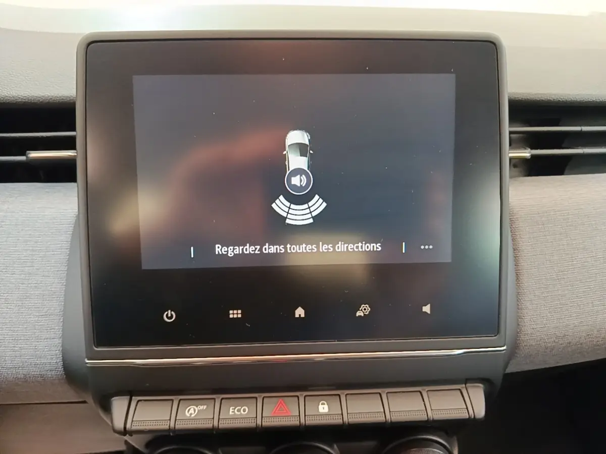 Écran tactile central de la Renault Clio gris clair affichant l'alerte de détection d'obstacles avec message "Regardez dans toutes les directions".