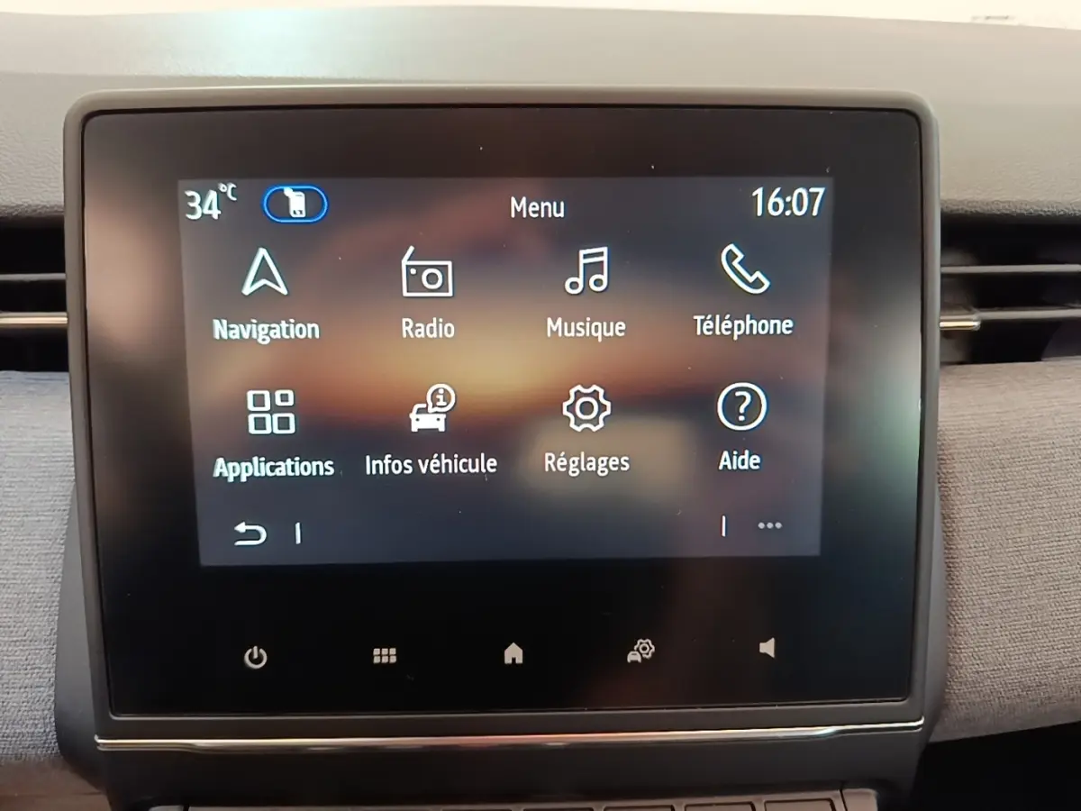 Écran tactile central du tableau de bord de la Renault Clio gris clair, affichant le menu principal avec navigation et radio.