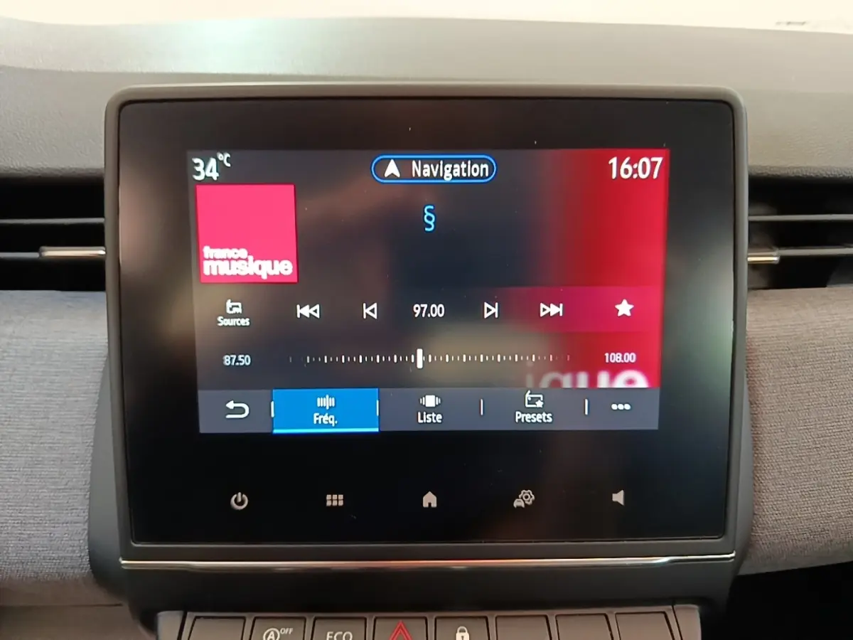 Écran tactile central de la Renault Clio gris clair, affichant la radio et la navigation, vue intérieure frontale.