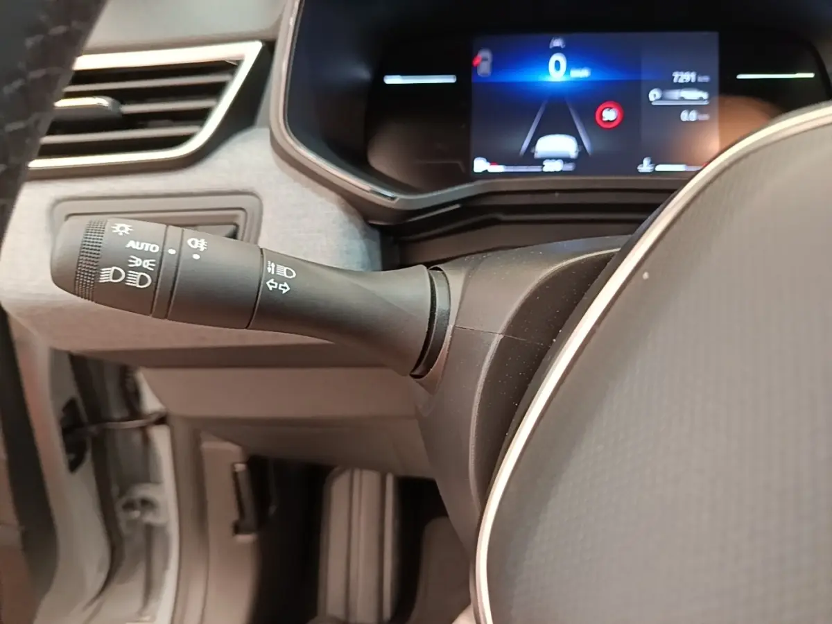 Vue rapprochée du commodo d’éclairage à gauche du volant cuir synthétique de la Renault Clio gris clair 2025.