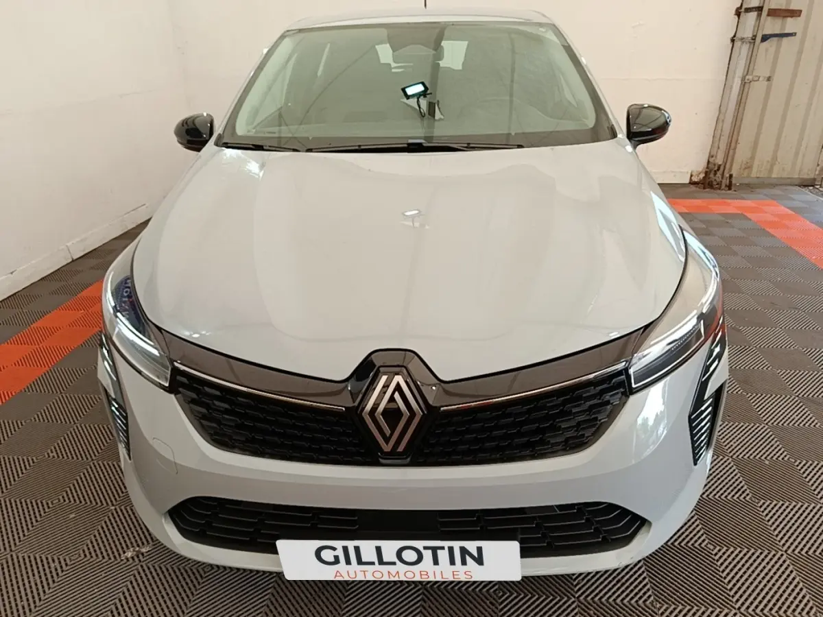 Vue avant de la Renault Clio gris clair 2025 avec calandre noire et phares LED allumés en intérieur.