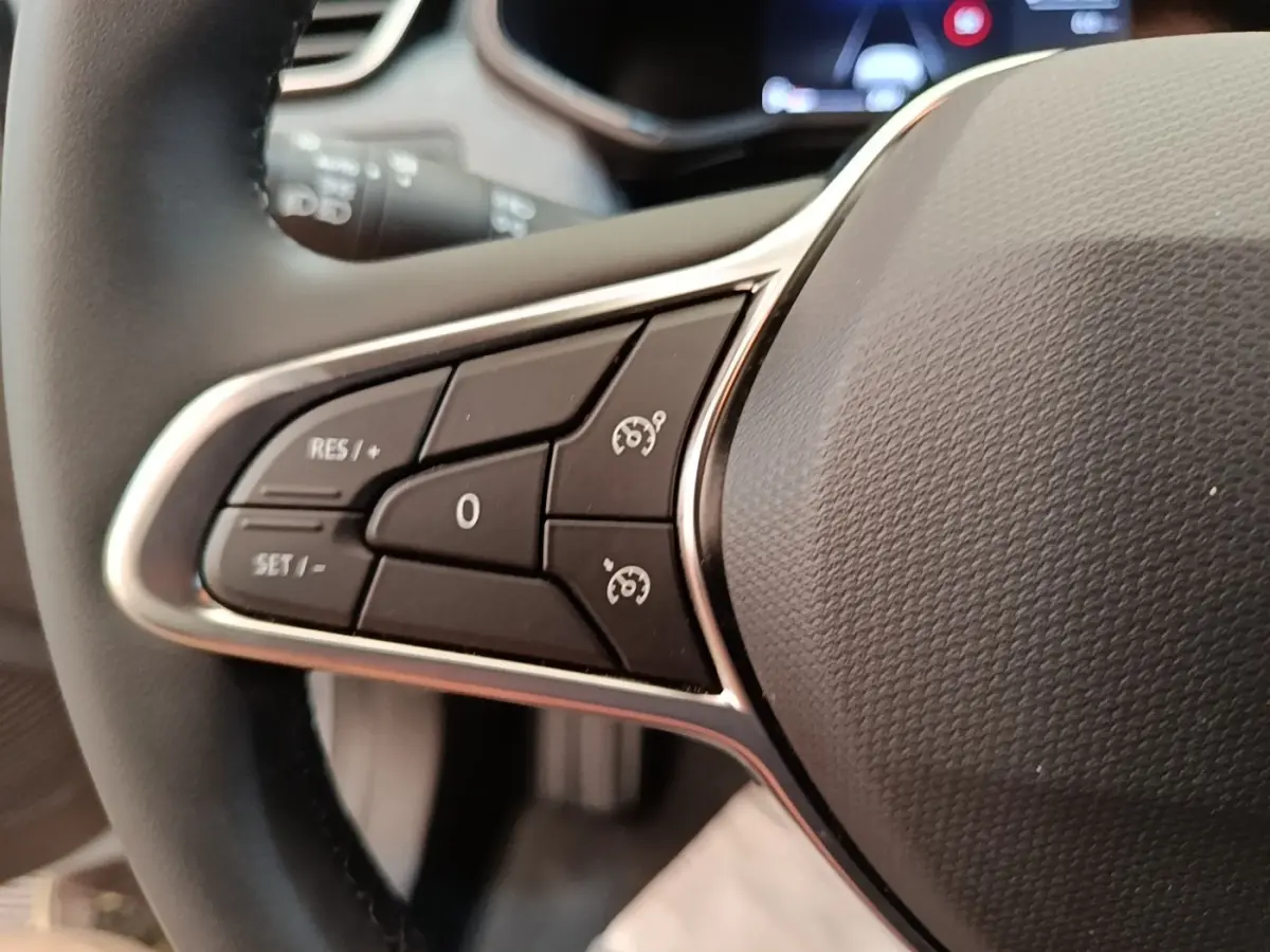 Gros plan sur les commandes du volant cuir synthétique de la Renault Clio gris clair, avec boutons de régulateur de vitesse.
