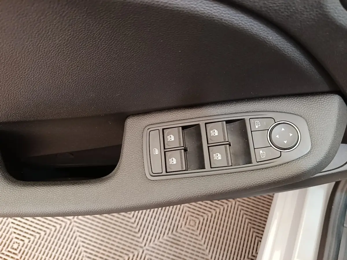 Gros plan sur la commande des vitres et rétroviseurs côté conducteur de la Renault Clio gris clair 2025.