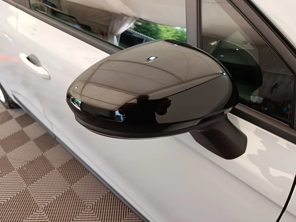 Gros plan sur le rétroviseur droit noir brillant d’une Renault Clio gris clair, vue latérale côté droit.