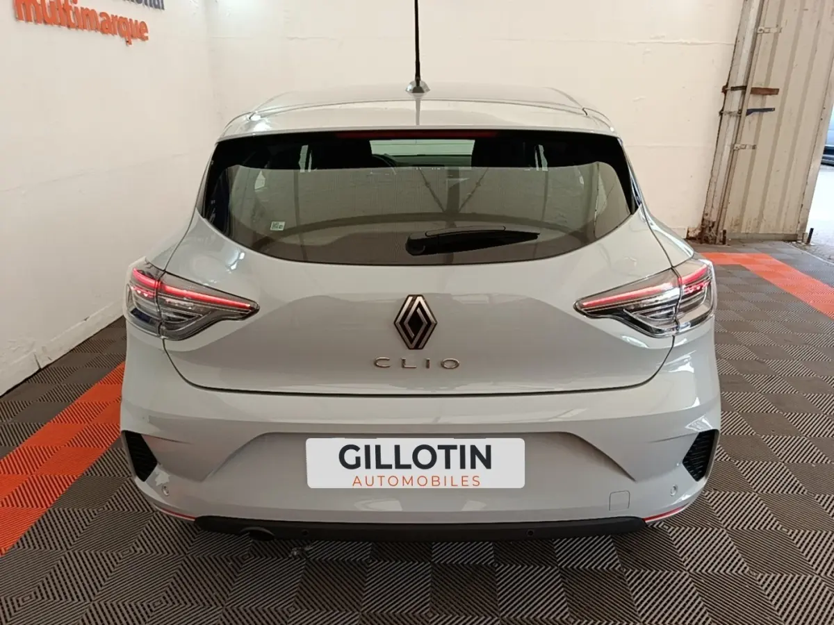 Vue arrière d'une Renault Clio gris clair 2025 avec feux LED et spoiler de toit visible en intérieur showroom.