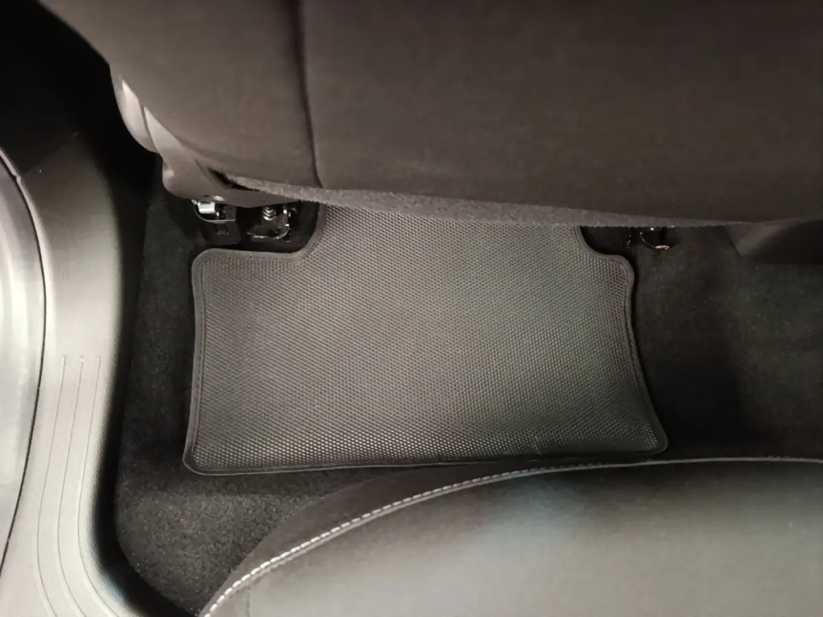 Vue intérieure du sol arrière côté droit de la Renault Clio gris clair, tapis de sol noir avec surpiqûres blanches visibles.