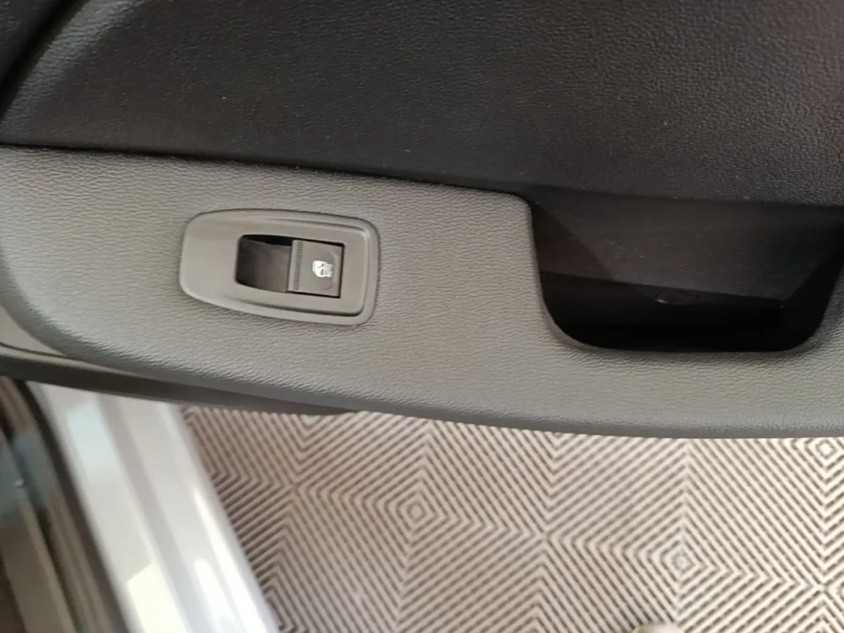 Gros plan sur le bouton de verrouillage de la porte intérieure d’une Renault Clio gris clair, vue côté conducteur.
