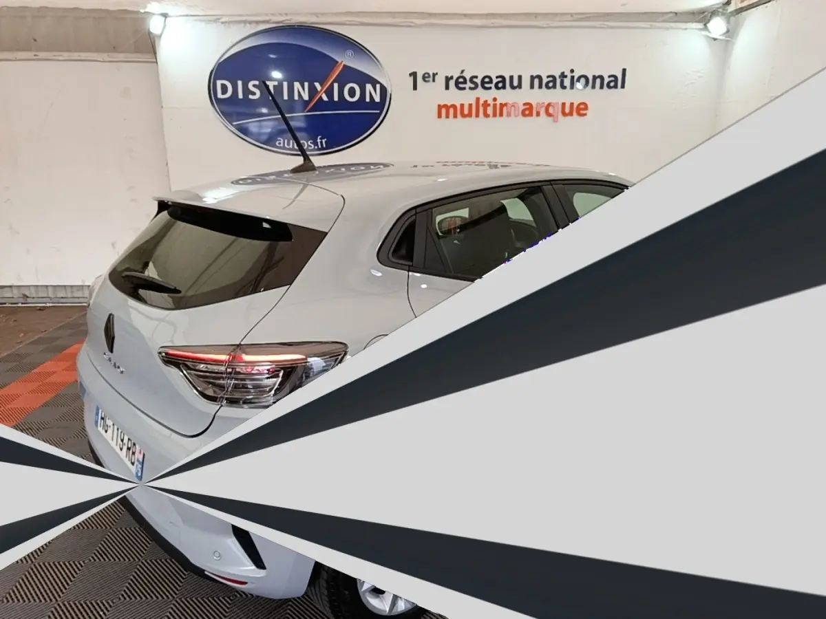 Vue 3/4 arrière d'une Renault Clio gris clair garée en intérieur, avec spoiler de toit et feux arrière LED visibles.