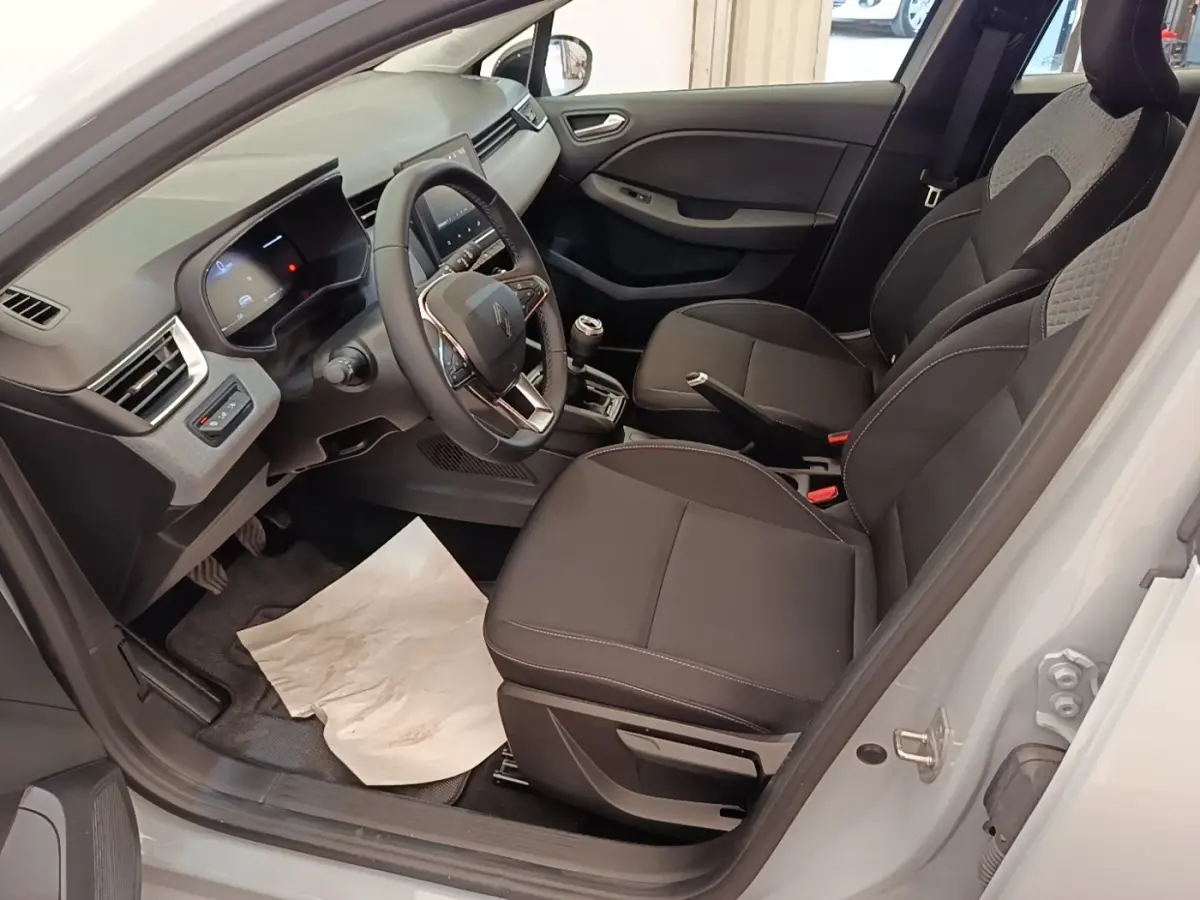 Vue intérieure côté conducteur de la Renault Clio gris clair 2025, volant cuir multifonctions et sièges tissu noirs.
