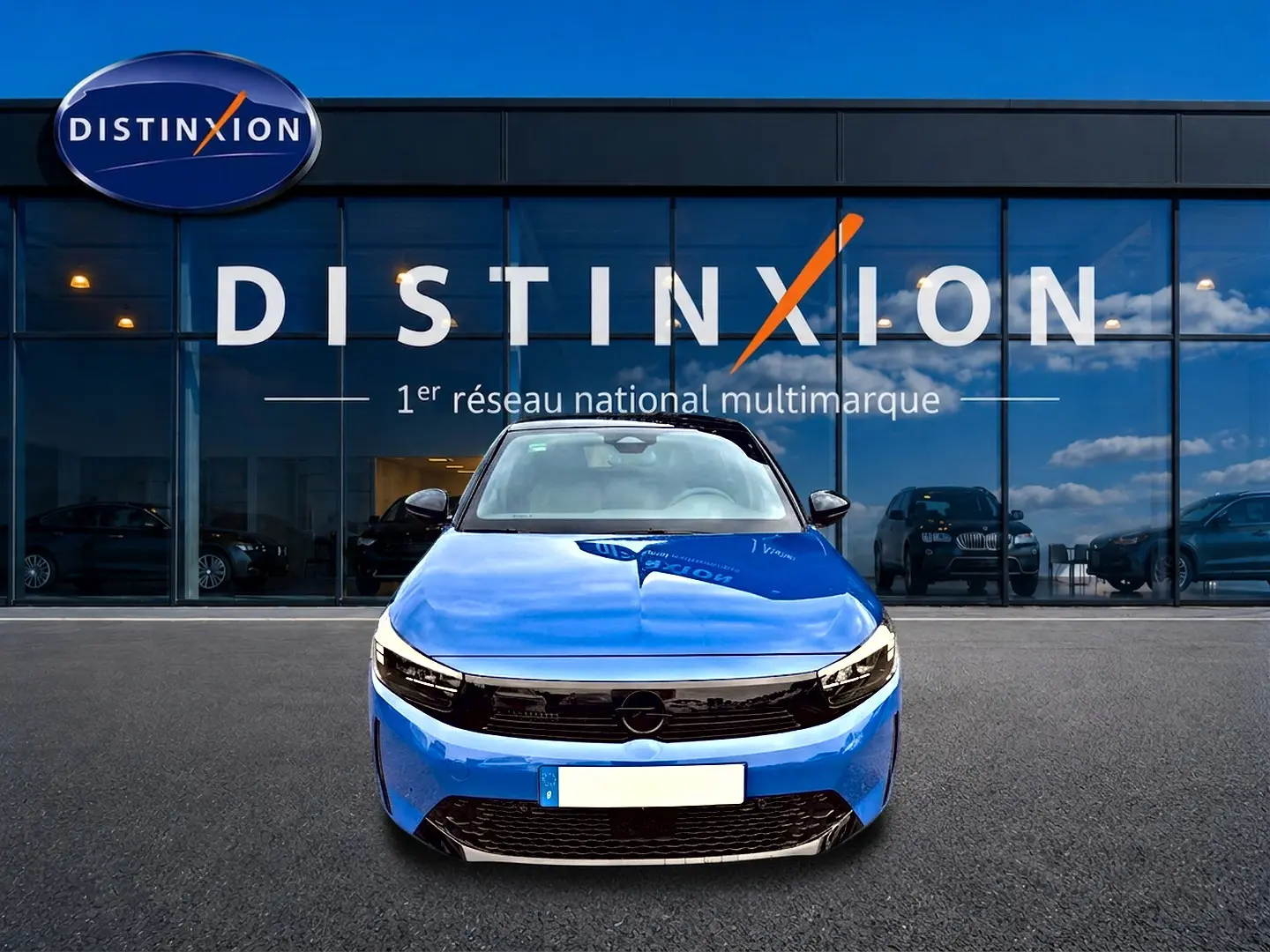 Vue frontale d'une Opel Corsa 1.2 turbo 100 gs bleu avec calandre noire et phares LED devant un showroom Distinxion.