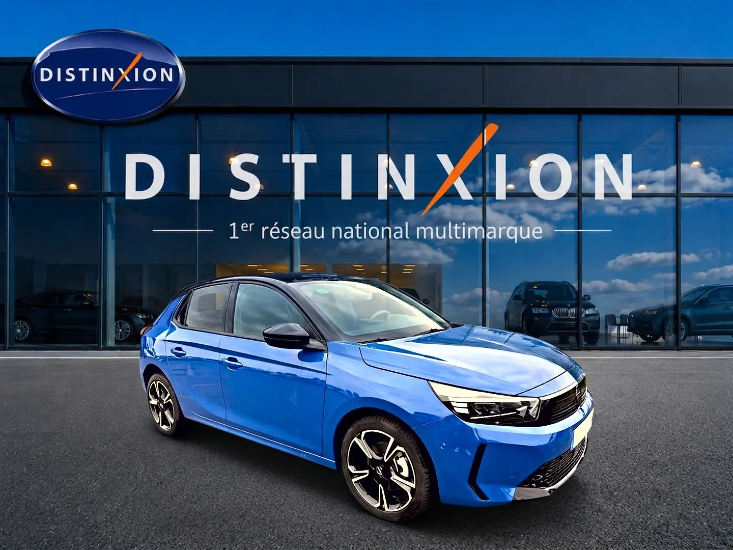 Opel Corsa 1.2 turbo bleu en 3/4 avant droit, jantes alu noires et phares LED visibles devant un showroom Distinxion.