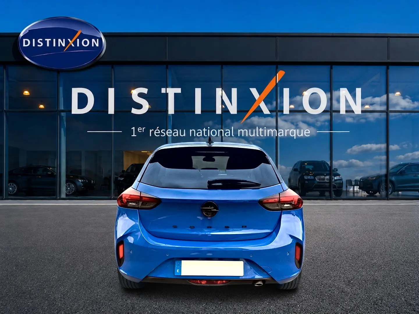 Vue arrière d'une Opel Corsa bleu vif garée devant une vitrine avec logo Distinxion.