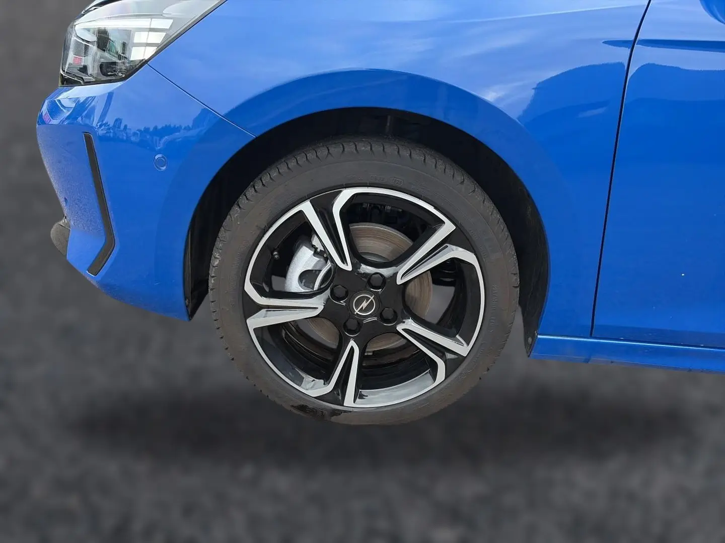 Gros plan sur la roue avant gauche et le pare-chocs bleu d'une Opel Corsa 1.2 turbo 100 GS avec jante alu noire et argent.