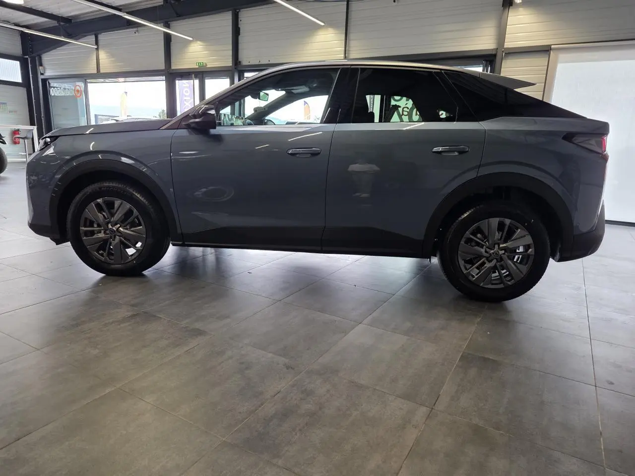 Profil côté gauche du Peugeot 3008 hybride bleu métallisé 2026 en intérieur, avec toit noir et jantes alliage.