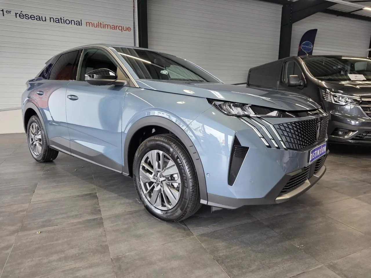 Peugeot 3008 hybride bleu vue 3/4 avant droit en intérieur, avec calandre noire laquée et jantes alliage 18 pouces.