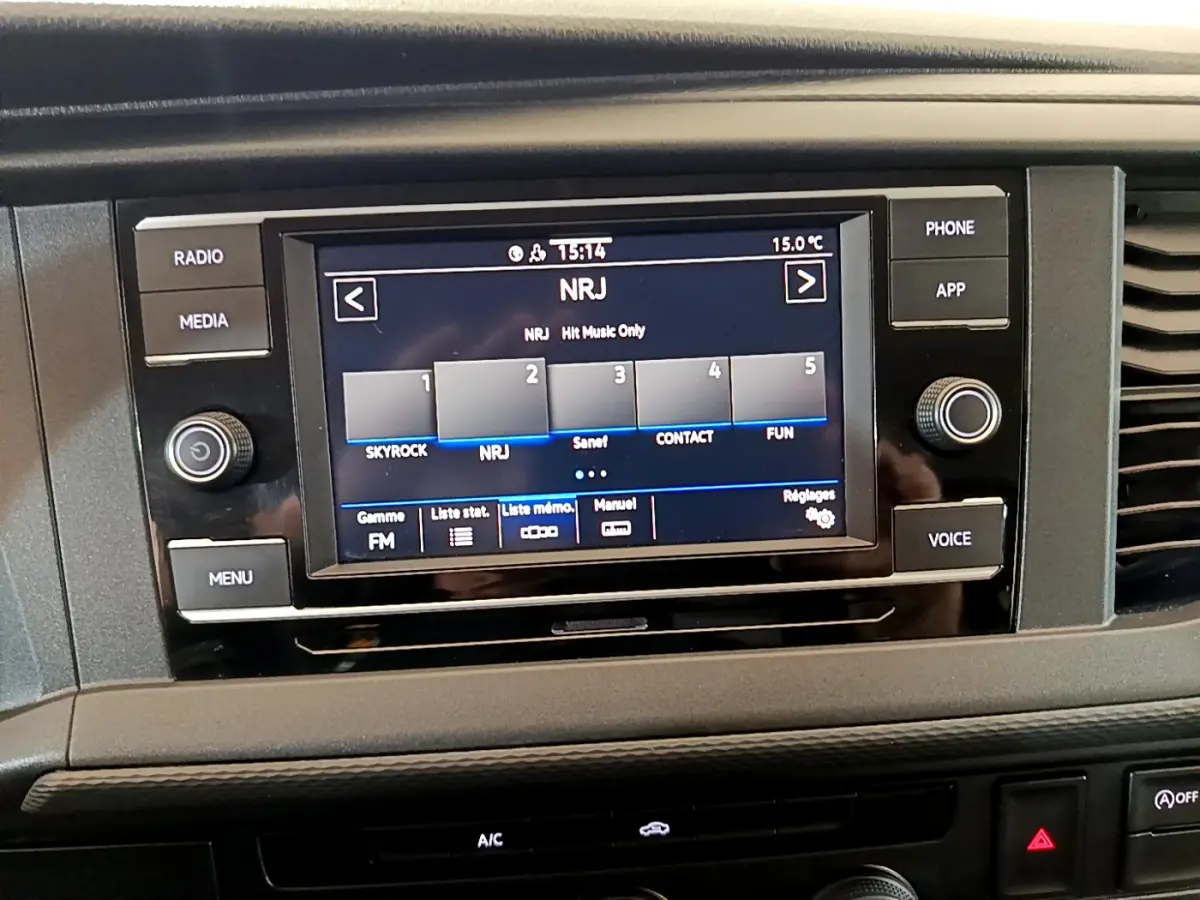 Écran tactile central du tableau de bord du Volkswagen Transporter blanc, affichant la radio NRJ en FM.