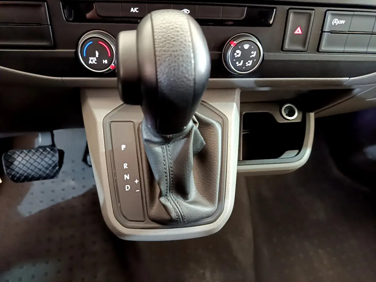 Le levier de vitesses automatique noir du Volkswagen Transporter 2.0 TDi 150 DSG7 avec commandes de climatisation en arrière-plan.