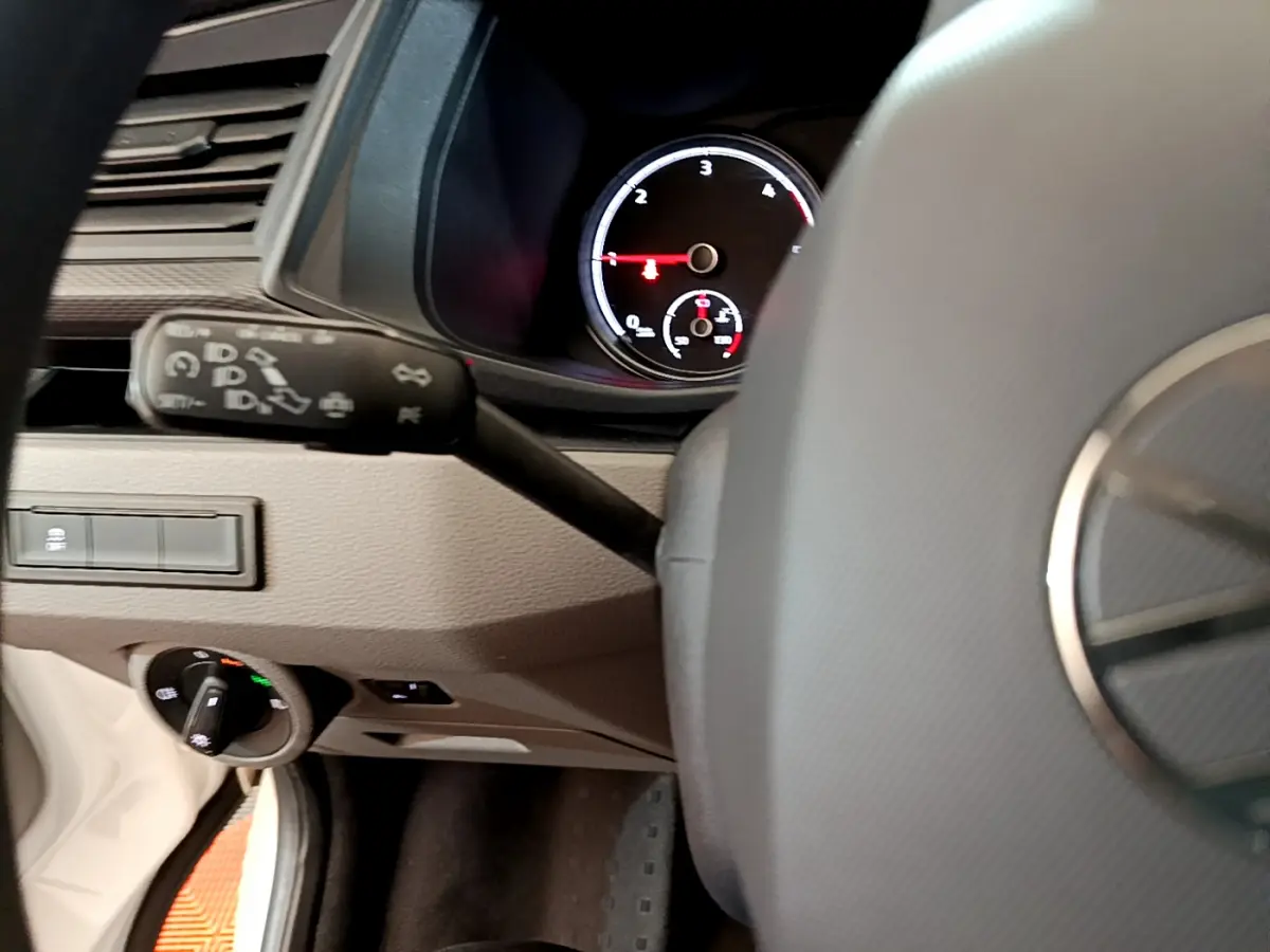 Vue partielle du tableau de bord et volant noir du Volkswagen Transporter blanc, avec compte-tours et commandes visibles.