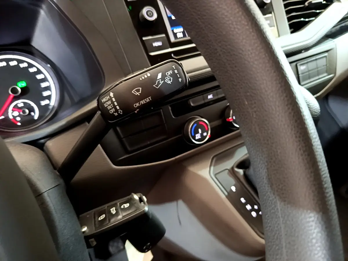 Gros plan sur le volant et la commande d'essuie-glace du Volkswagen Transporter blanc, tableau de bord et console visibles.