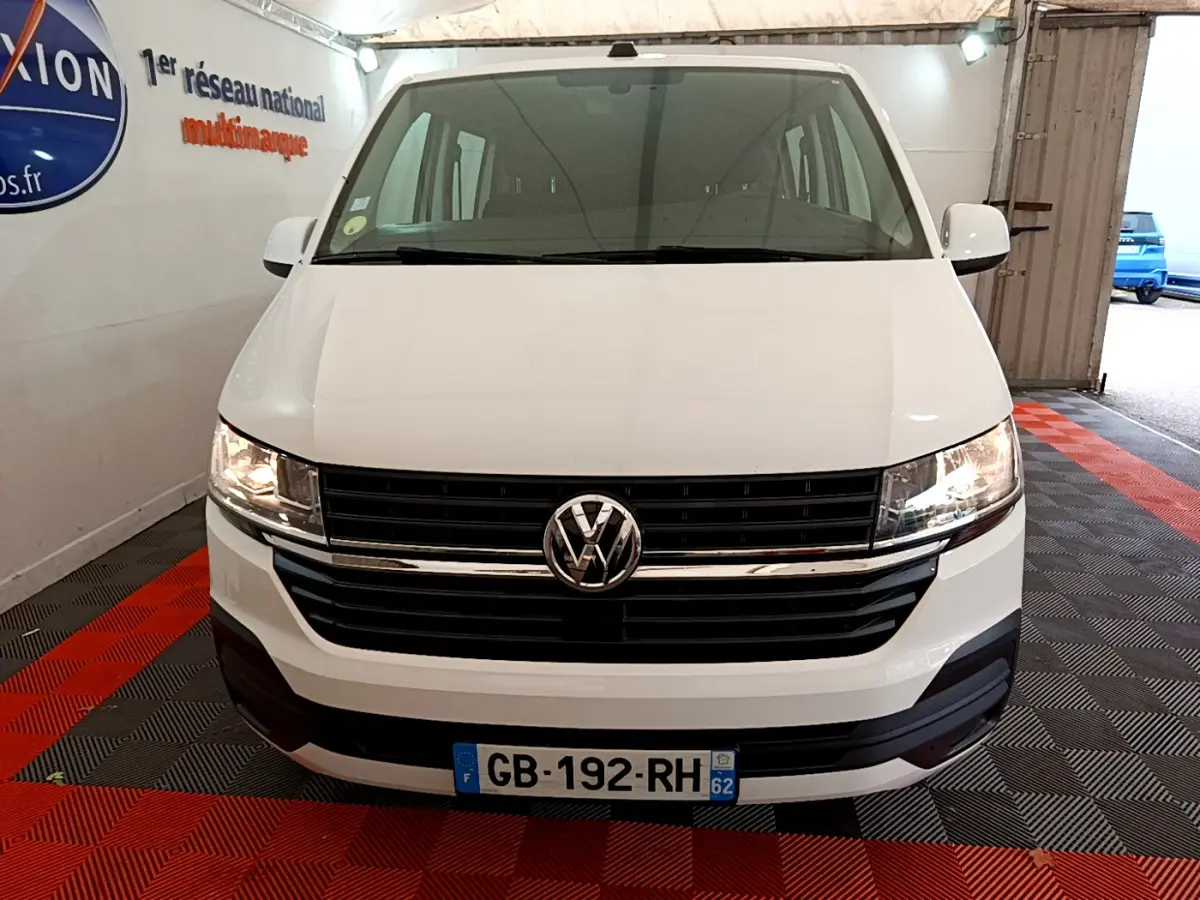 Vue frontale d'un Volkswagen Transporter blanc 2021 avec calandre noire et phares allumés dans un garage.