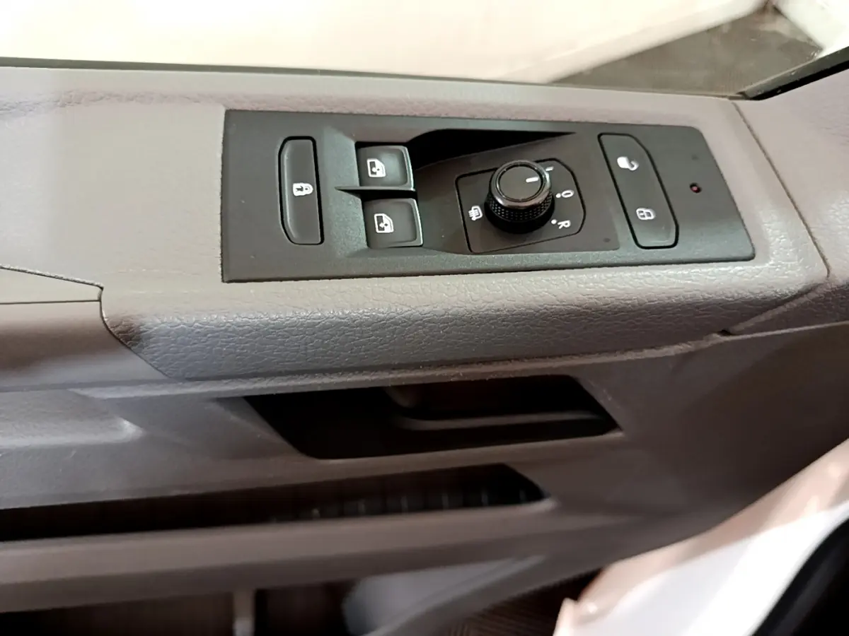 Gros plan sur les commandes de lève-vitres et réglage des rétroviseurs côté conducteur du Volkswagen Transporter blanc 2021.