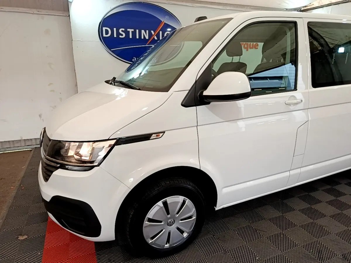 Vue 3/4 avant droite du Volkswagen Transporter blanc 2021 avec phares allumés et jantes acier.