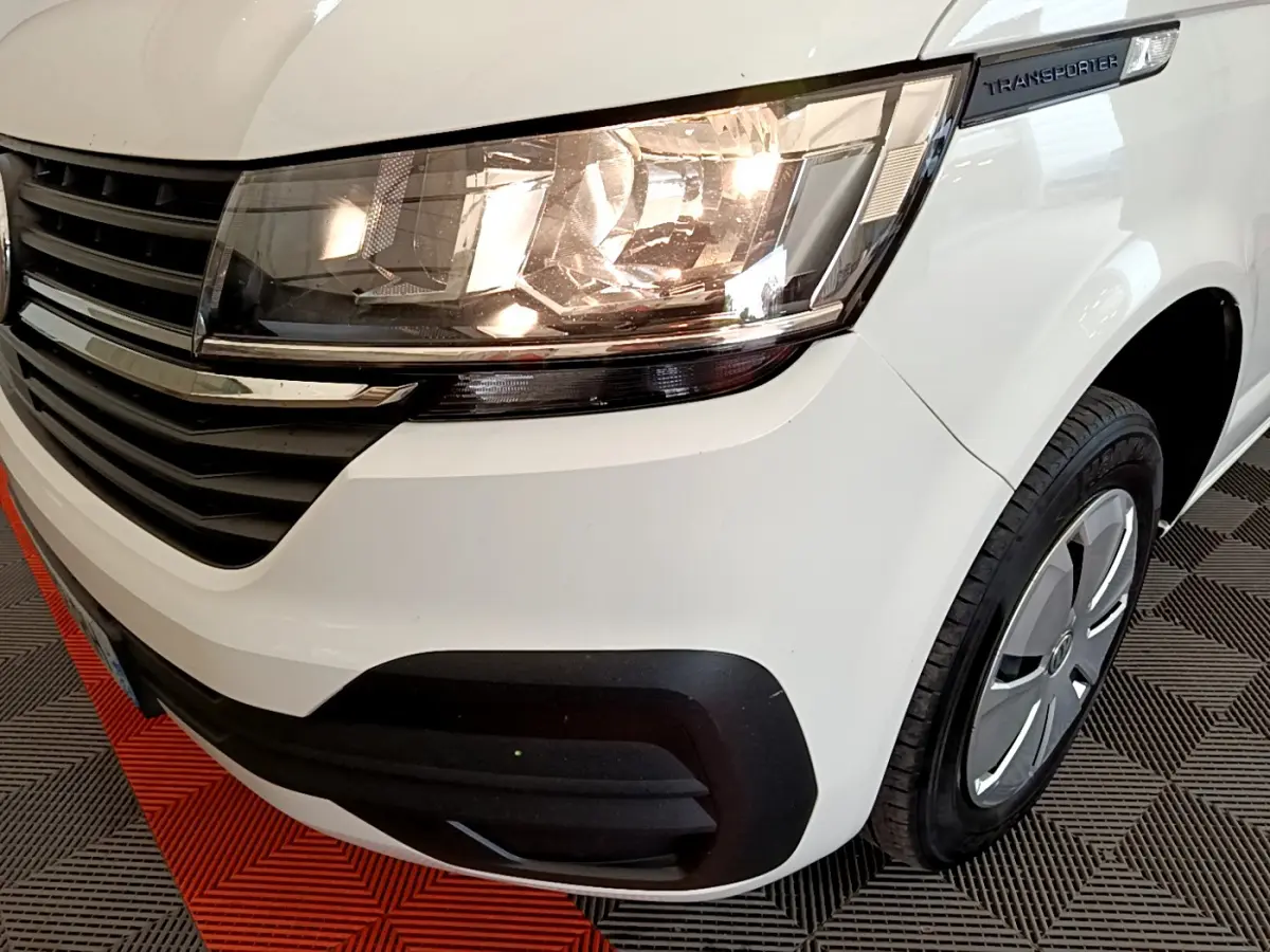 Gros plan sur l'avant droit blanc du Volkswagen Transporter 2.0 TDi 150 avec phare allumé et calandre noire.