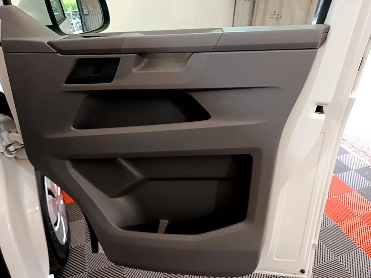 Vue rapprochée de la porte intérieure grise côté conducteur du Volkswagen Transporter blanc 2021, avec poignée intégrée.