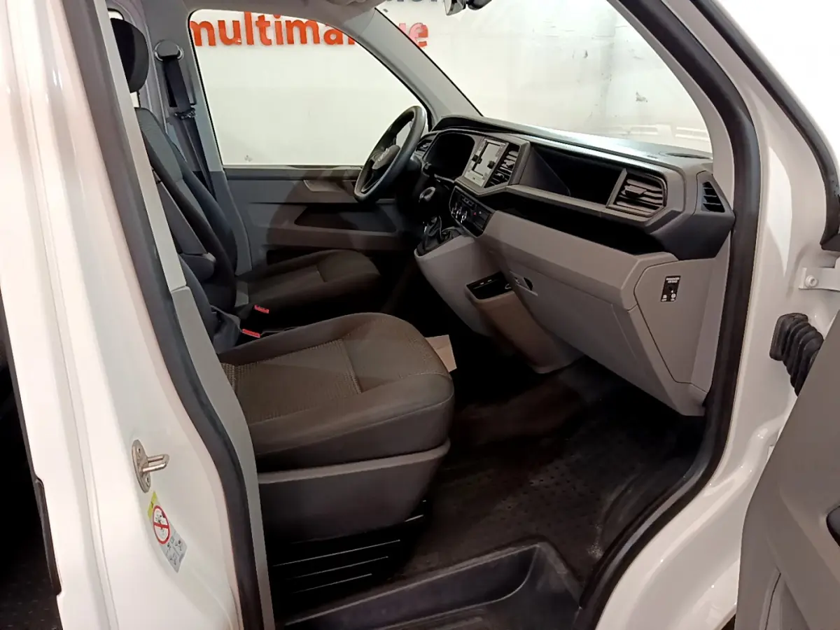 Intérieur côté conducteur du Volkswagen Transporter blanc 2021, montrant sièges et tableau de bord moderne.