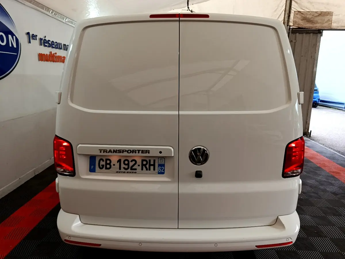 Vue arrière du Volkswagen Transporter blanc avec portes battantes fermées et feux rouges allumés dans un garage.