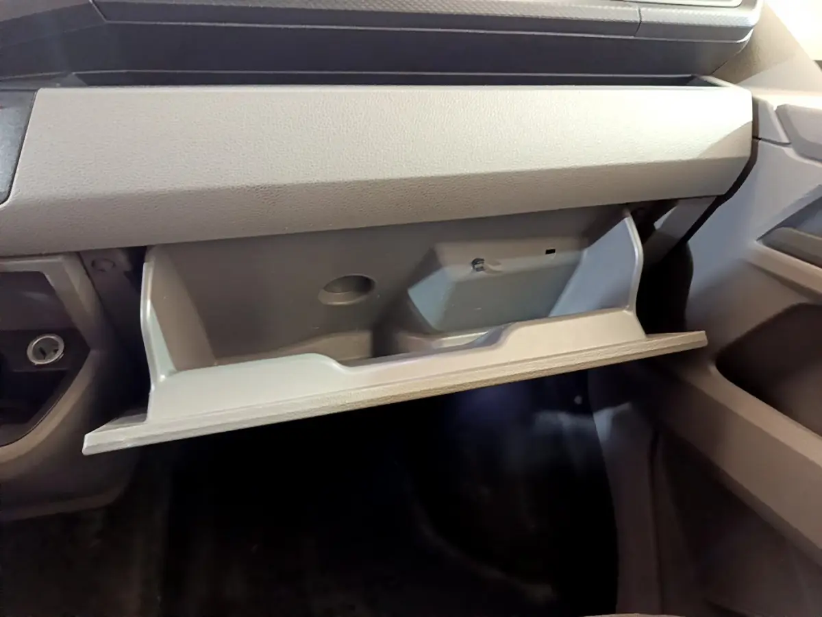 Vue rapprochée de la boîte à gants ouverte côté passager dans l'habitacle gris du Volkswagen Transporter blanc.
