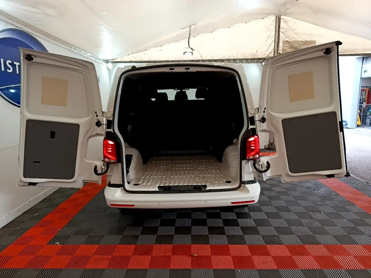 Vue arrière d'un Volkswagen Transporter blanc 2021 avec portes battantes ouvertes montrant l'espace de chargement vide.