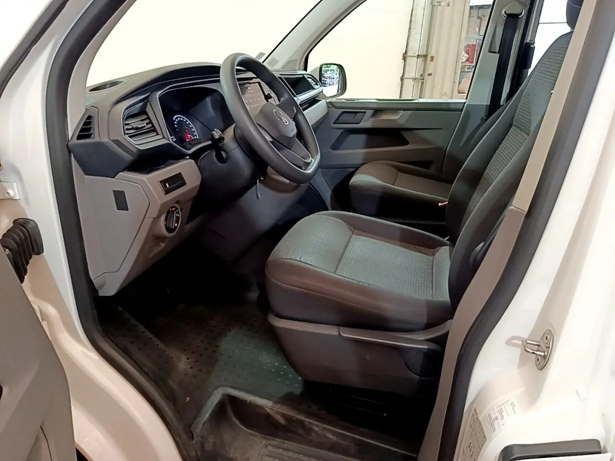 Intérieur côté conducteur du Volkswagen Transporter blanc, montrant le tableau de bord et les sièges avant gris foncé.