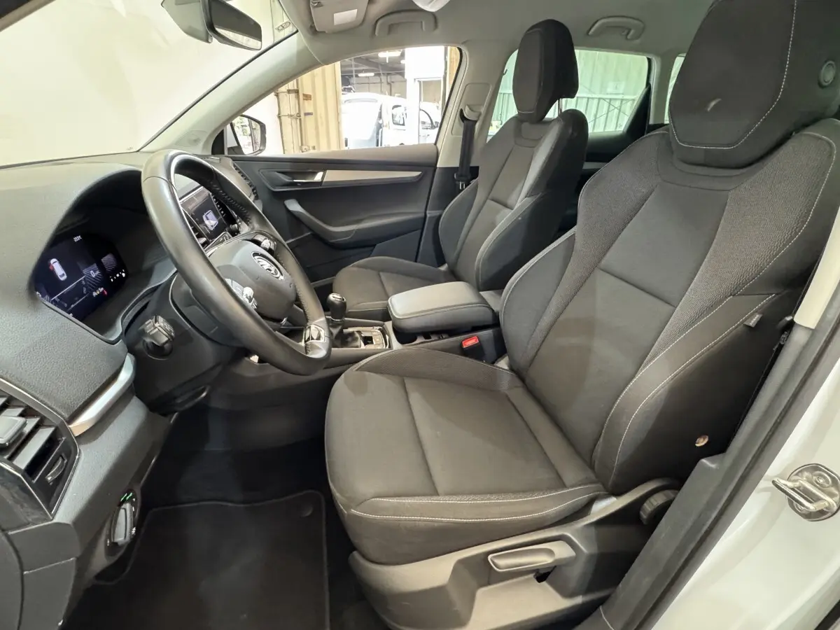 Intérieur vue côté conducteur du Skoda Karoq blanc 2024, sièges tissu noirs et volant cuir multifonctions.