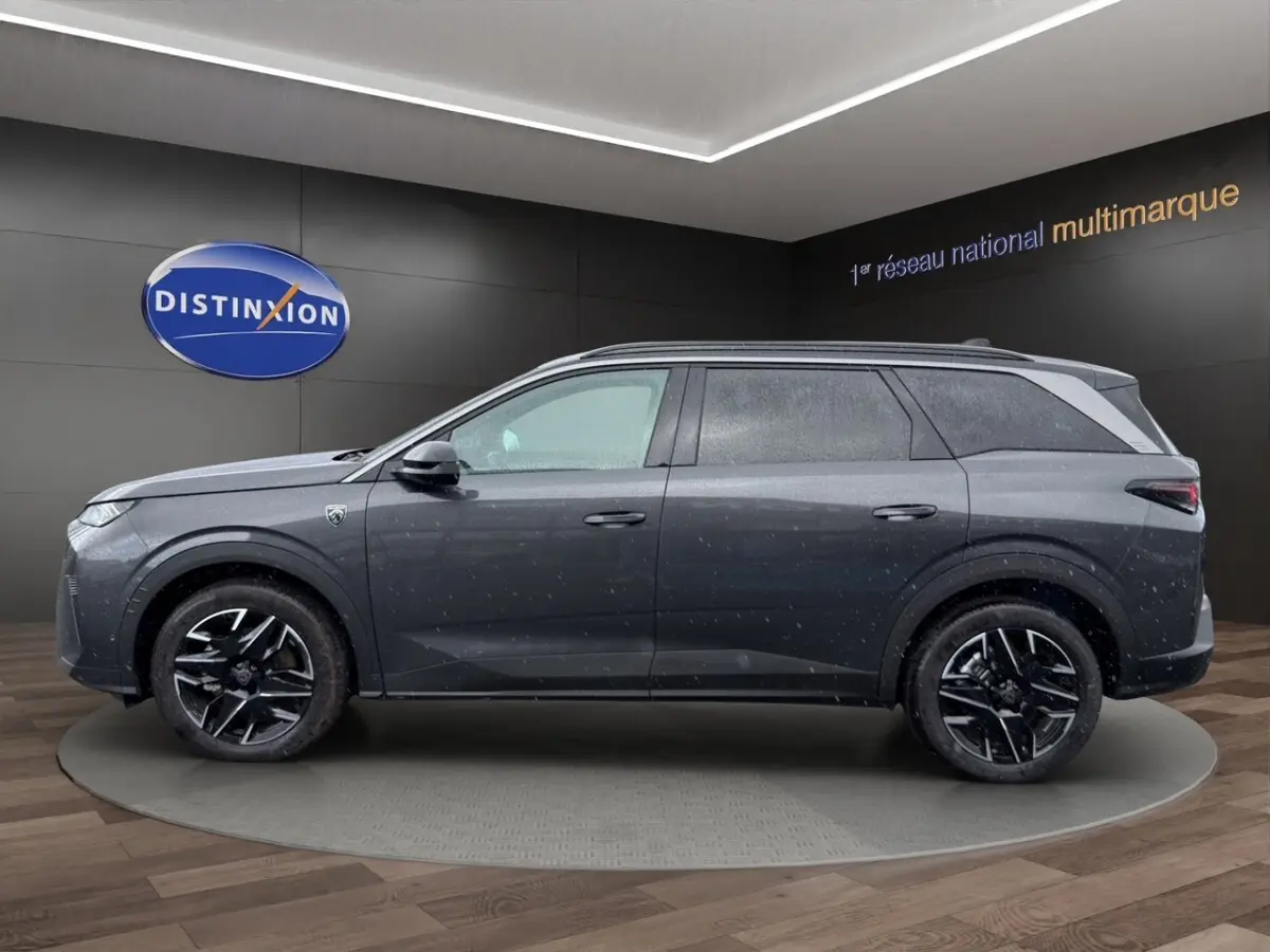 Vue latérale droite d’un Peugeot 5008 gris foncé avec jantes noires et toit surélevé en showroom.