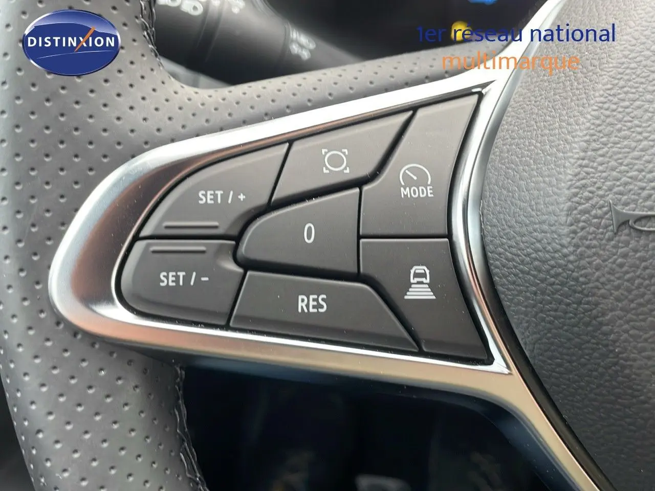 Gros plan sur les commandes du volant perforé du Renault Captur blanc nacré, version hybride 2025, avec boutons multifonctions.