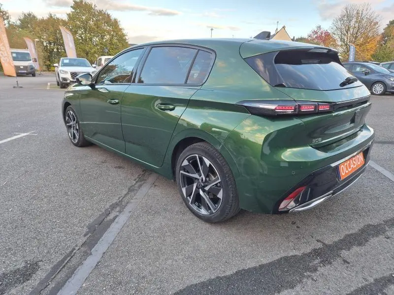 PEUGEOT 308 vert olivine vue 3/4 arrière droit, jantes alu et feux arrière LED allumés sur parking extérieur.