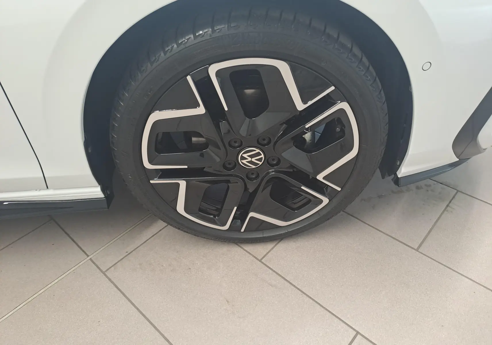 Gros plan sur la roue avant gauche d'une Volkswagen Golf blanche avec jante noire et détails argentés au design moderne.