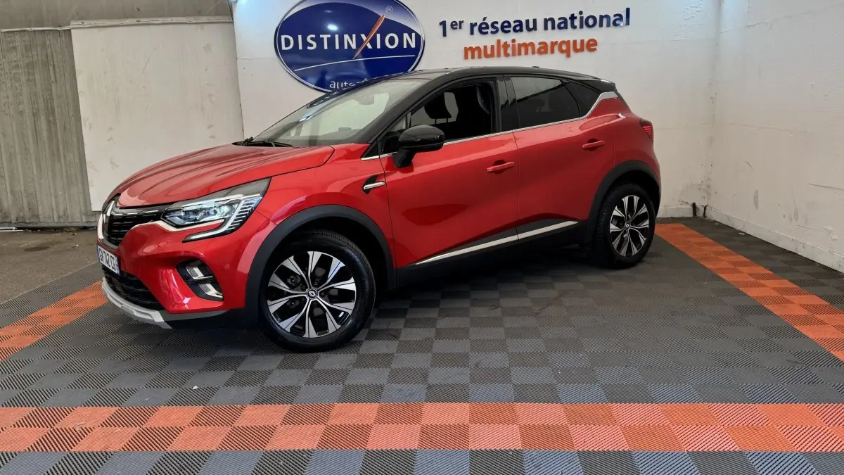 Renault Captur rouge en 3/4 avant droit, toit noir, jantes alliage et feux LED visibles en intérieur showroom.
