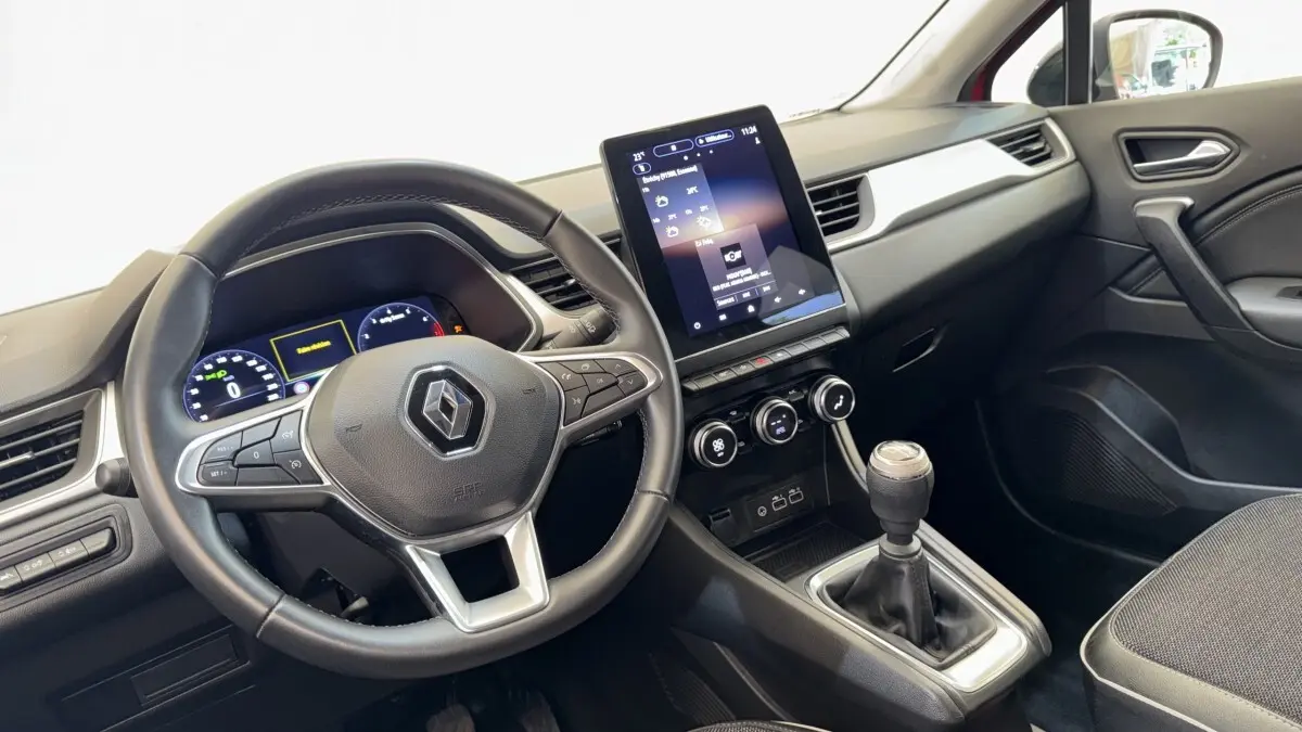 Vue intérieure du tableau de bord et volant du Renault Captur rouge 2024 avec écran tactile vertical et boîte manuelle.