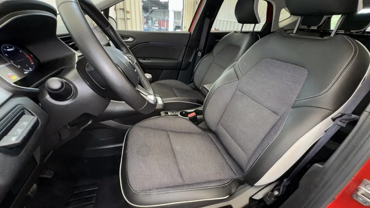 Vue intérieure côté conducteur du Renault Captur rouge 2024, sièges tissu et cuir avec volant multifonctions.
