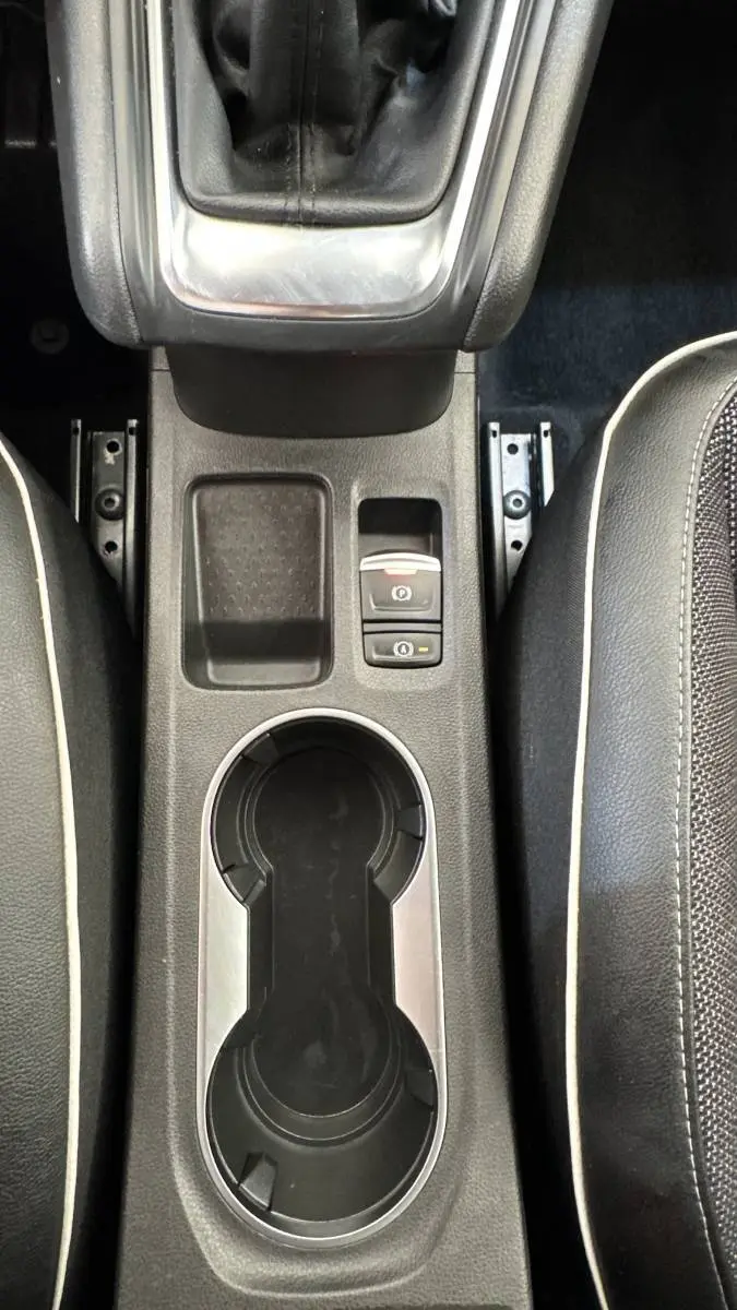 Vue plongeante sur la console centrale noire du Renault Captur rouge 2024, avec frein à main électrique et porte-gobelets.