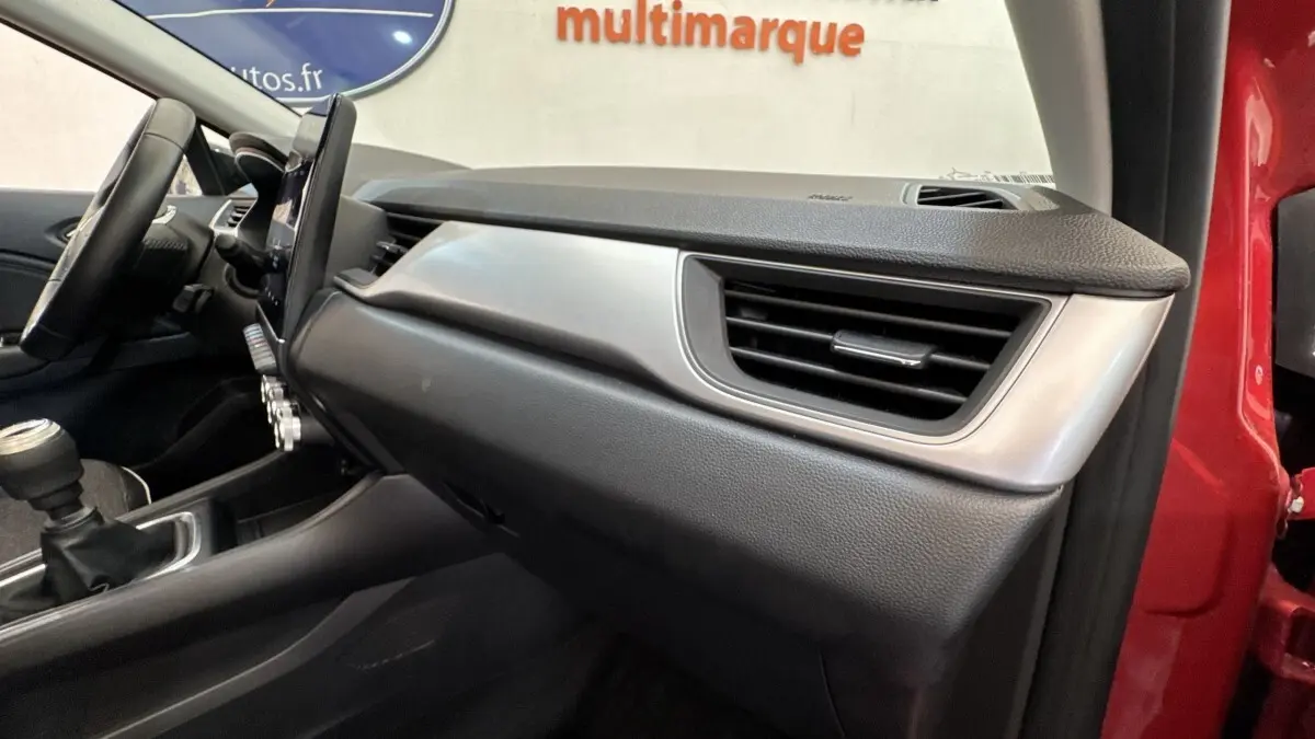 Intérieur côté passager du Renault Captur rouge 2024, tableau de bord moderne avec écran tactile vertical et boîte manuelle.