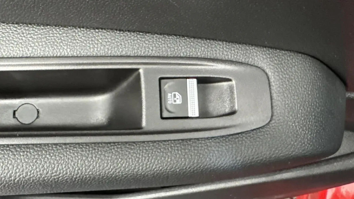 Gros plan sur le bouton de commande de la vitre électrique avant dans l'habitacle d'un Renault Captur rouge 2024.