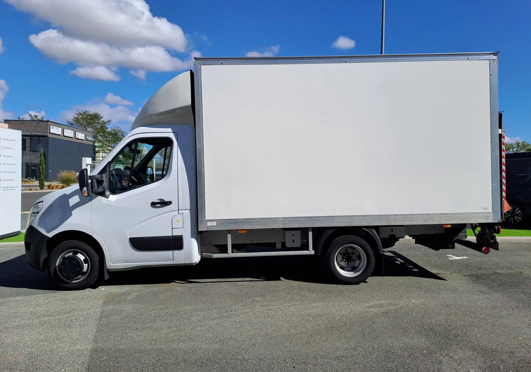 Vue de profil côté gauche d’un utilitaire blanc Nissan Interstar Châssis Cabine L3H1 avec caisse fermée sur fond urbain.