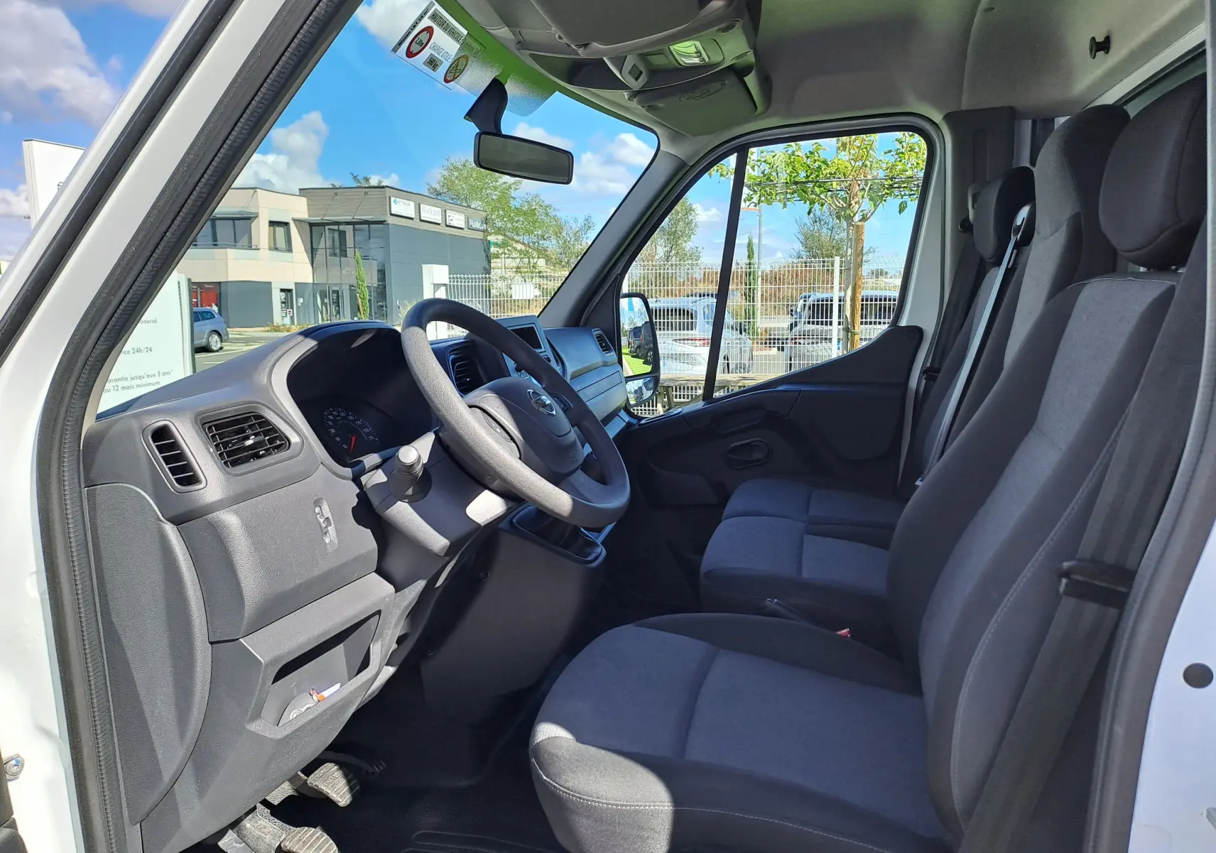 Vue intérieure côté conducteur du Nissan Interstar blanc 2024, montrant le tableau de bord et les sièges en tissu noir.
