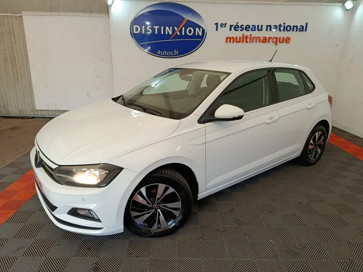 Volkswagen Polo blanc vue 3/4 avant droit en intérieur avec jantes alliage et phares allumés.